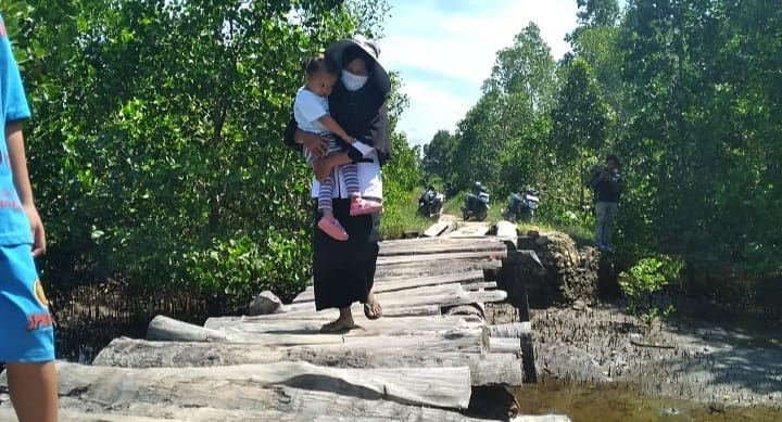 Nurbaya (Guru Kontrak) menggendong anaknya saat melewati jembatan rapih untuk bisa sampai di sekolah tempatnya mengajar